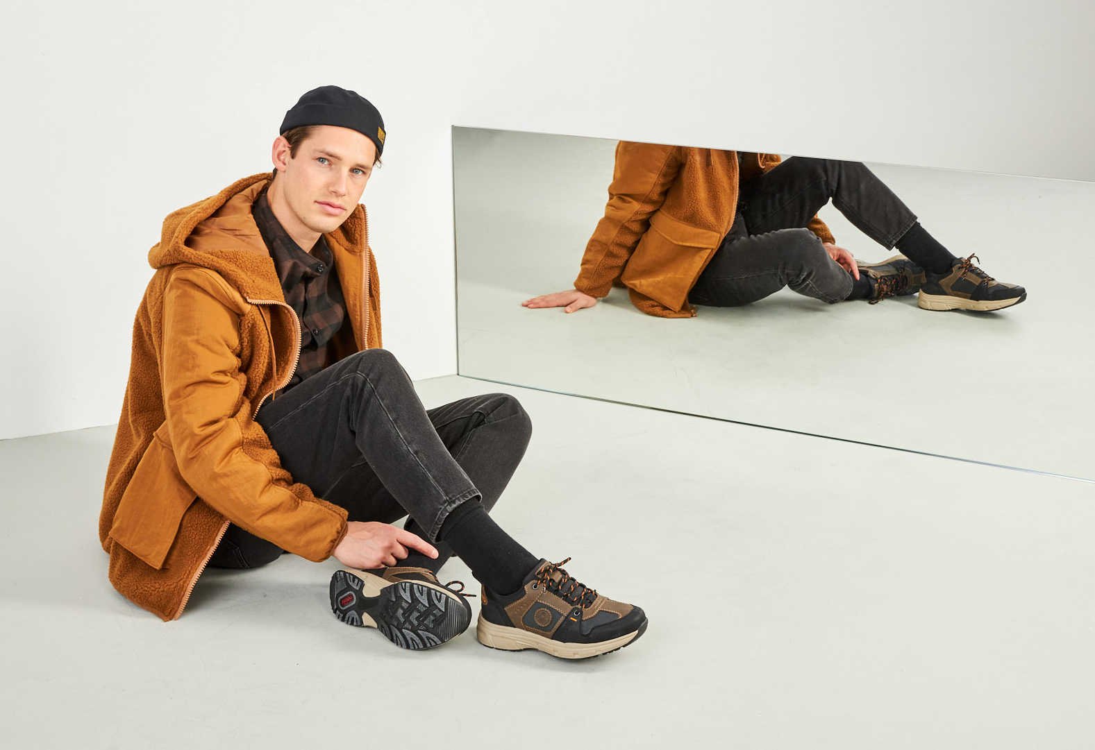 Ein junger Mann sitzt von einem Spiegel und präsentiert seine Schuhe