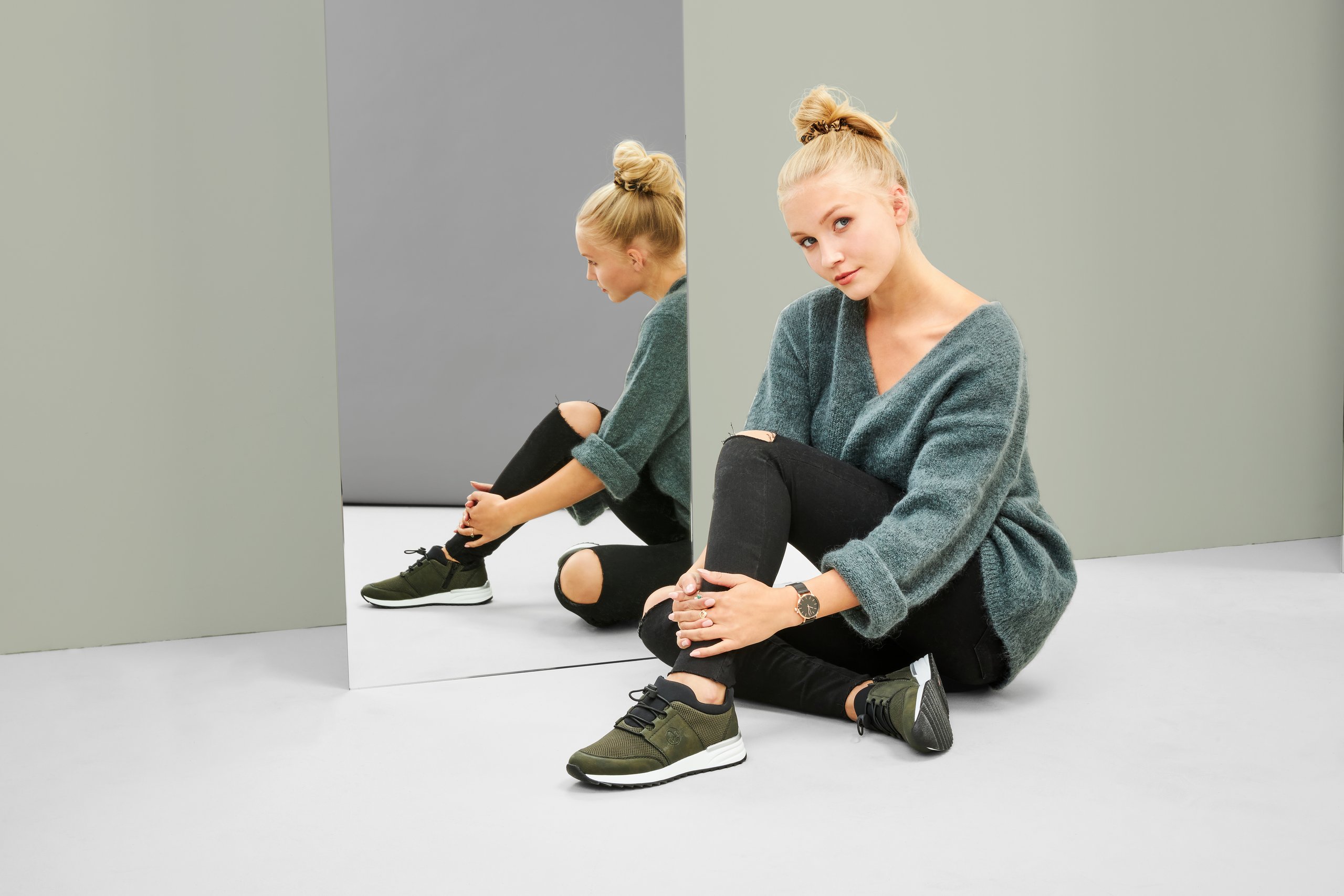 Eine junge Frau sitzt vor einem Spiegel und präsentiert ihre dunkelgrauen Sneaker